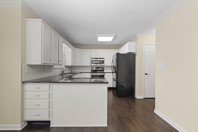 kitchen with white cabinets, dark countertops, appliances with stainless steel finishes, a peninsula, and a sink