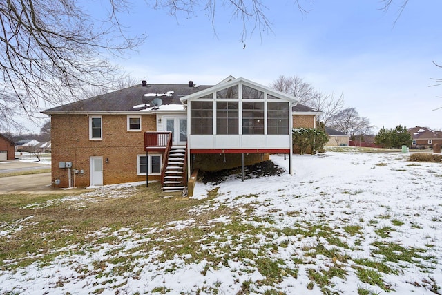 snow covered house with stairs, brick siding, and a sunroom