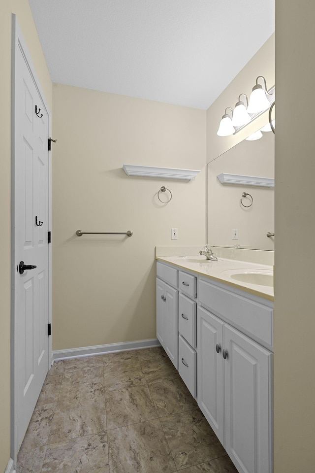 full bathroom with double vanity, a sink, and baseboards