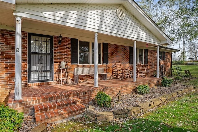 doorway to property featuring a porch and brick siding