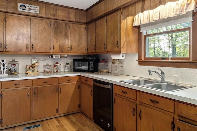 kitchen with light wood finished floors, visible vents, light countertops, black appliances, and a sink