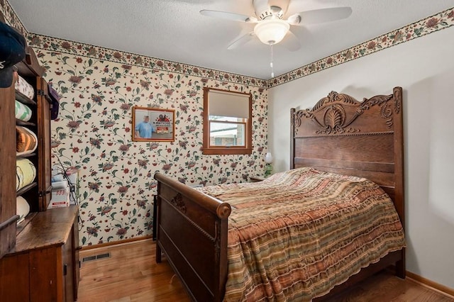 bedroom with wallpapered walls, baseboards, visible vents, ceiling fan, and wood finished floors