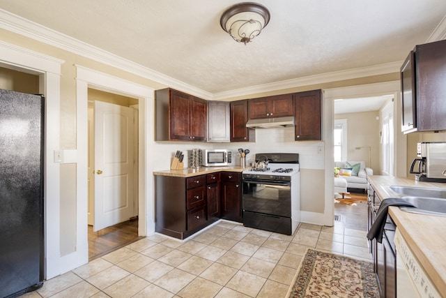 kitchen with under cabinet range hood, light countertops, freestanding refrigerator, stainless steel microwave, and range with gas cooktop