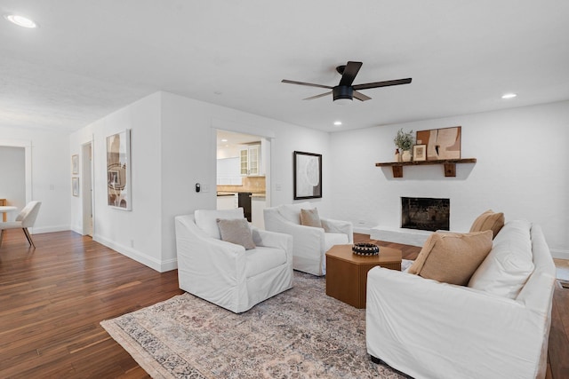 living room featuring a fireplace with raised hearth, dark wood-type flooring, baseboards, and recessed lighting