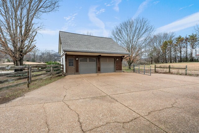 view of side of home featuring a shingled roof, an outbuilding, a detached garage, and fence