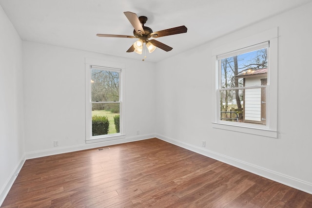 empty room with a ceiling fan, visible vents, dark wood finished floors, and baseboards