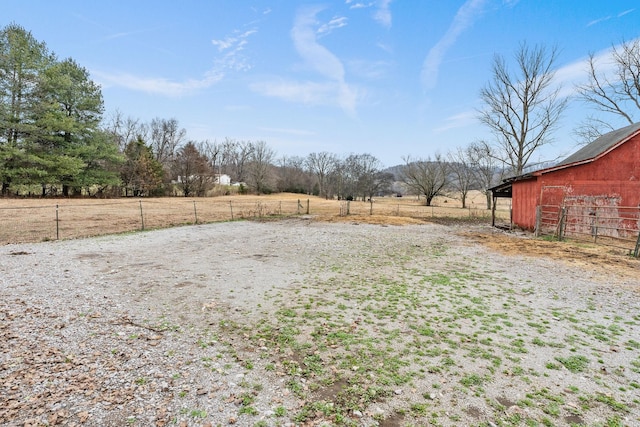 view of yard featuring a barn, a rural view, an outdoor structure, and fence