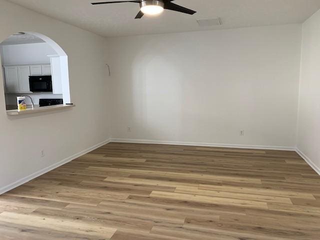 unfurnished room with arched walkways, ceiling fan, baseboards, and wood finished floors