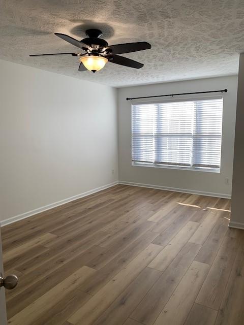 unfurnished room featuring ceiling fan, a textured ceiling, baseboards, and wood finished floors