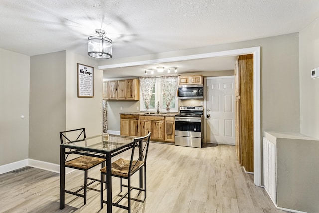 kitchen featuring appliances with stainless steel finishes, a sink, light wood-style flooring, and baseboards