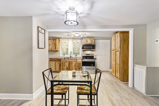 kitchen with light wood-style flooring, a sink, baseboards, light countertops, and appliances with stainless steel finishes