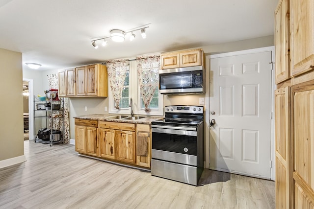 kitchen with light wood finished floors, appliances with stainless steel finishes, a sink, and baseboards