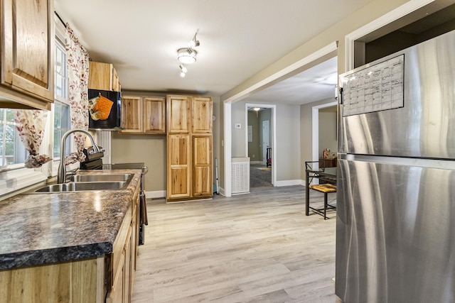 kitchen with dark countertops, light wood-style flooring, freestanding refrigerator, a sink, and baseboards