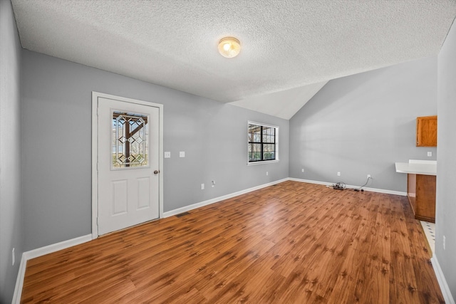 foyer entrance with a textured ceiling, wood finished floors, visible vents, baseboards, and vaulted ceiling