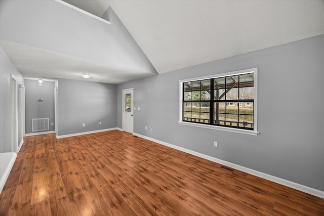 empty room with high vaulted ceiling, wood finished floors, visible vents, and baseboards