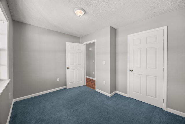 unfurnished bedroom with baseboards, dark carpet, and a textured ceiling