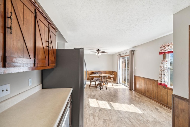 kitchen with brown cabinets, freestanding refrigerator, wainscoting, a textured ceiling, and wooden walls