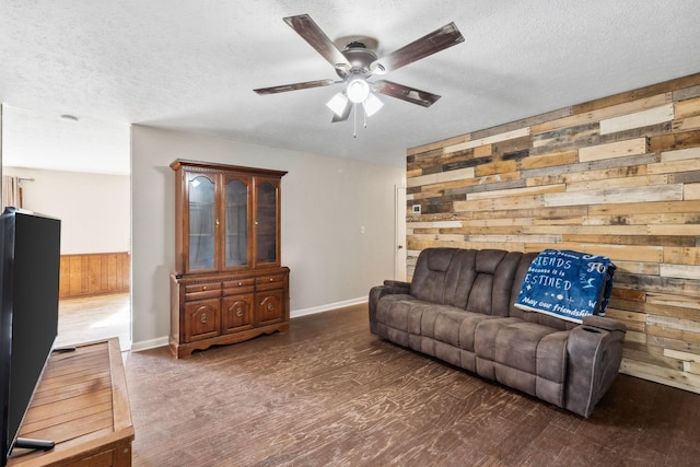 living area with ceiling fan, wood walls, a textured ceiling, and wood finished floors