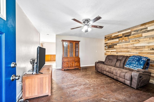 living area with a ceiling fan, wooden walls, a textured ceiling, and wood finished floors