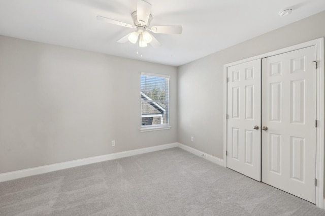 unfurnished bedroom with a closet, light colored carpet, ceiling fan, and baseboards