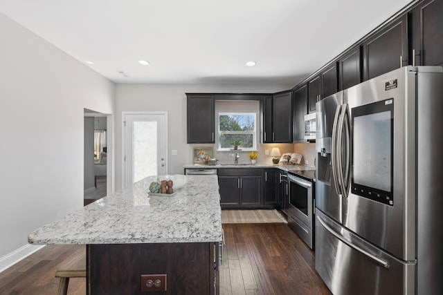 kitchen with a breakfast bar, dark wood finished floors, appliances with stainless steel finishes, a sink, and light stone countertops