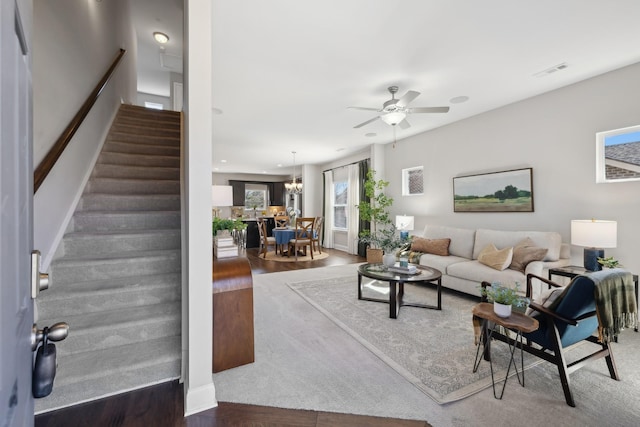 living room featuring stairs, visible vents, wood finished floors, and ceiling fan with notable chandelier