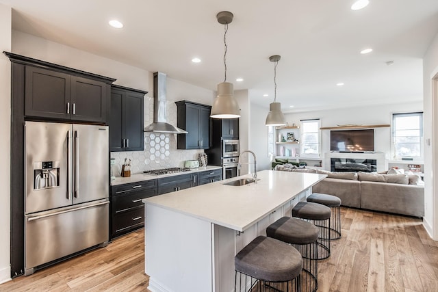 kitchen featuring a breakfast bar, decorative light fixtures, stainless steel appliances, light countertops, and wall chimney range hood