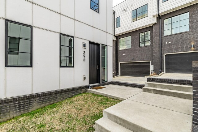 view of exterior entry featuring driveway, a garage, and brick siding