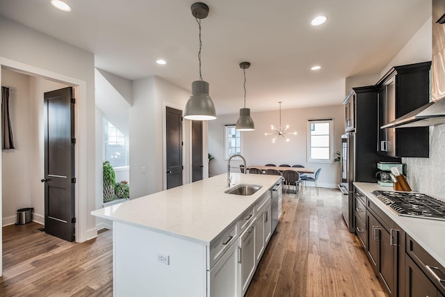 kitchen featuring an island with sink, decorative light fixtures, light wood-type flooring, wall chimney range hood, and a sink