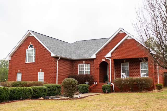 view of front facade with a shingled roof, brick siding, and a front lawn