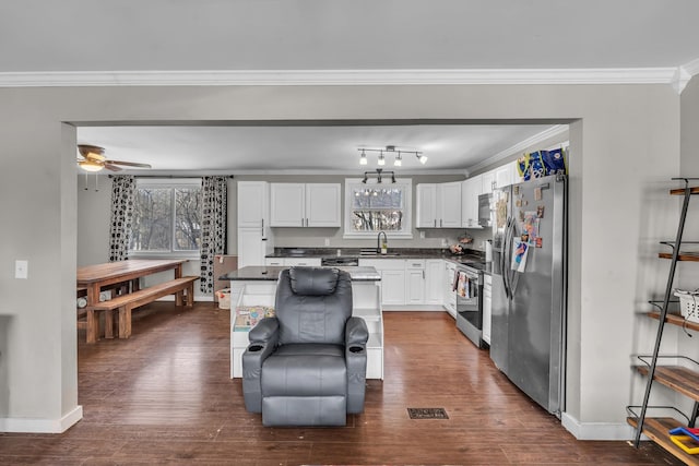 kitchen with a sink, white cabinets, appliances with stainless steel finishes, a center island, and dark countertops