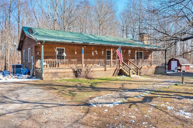 chalet / cabin with metal roof, a porch, an outdoor structure, a storage unit, and a chimney