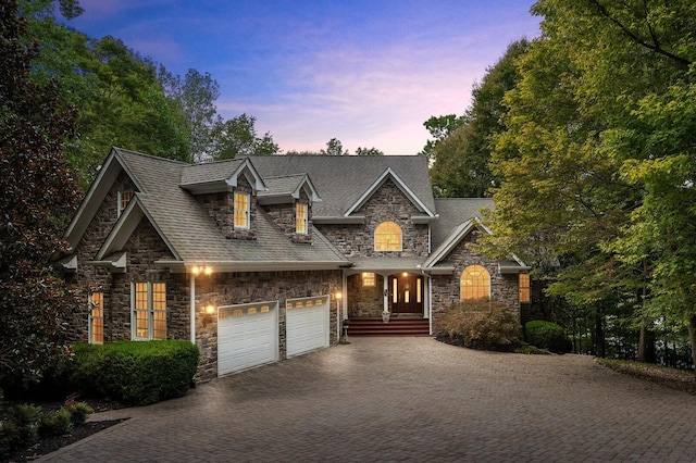 view of front of home with stone siding, decorative driveway, a shingled roof, and an attached garage