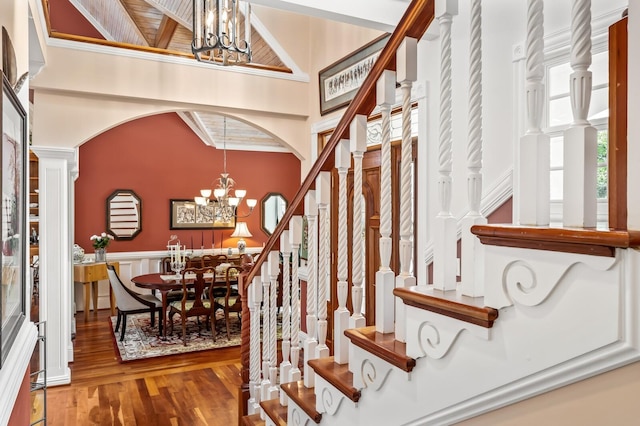 interior space with arched walkways, a notable chandelier, a towering ceiling, wood finished floors, and stairs