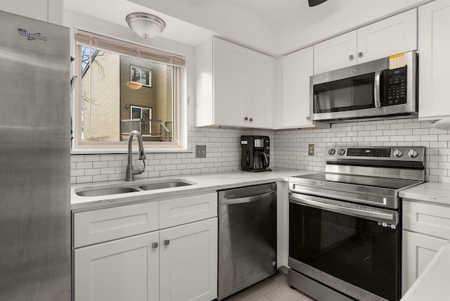 kitchen featuring tasteful backsplash, light stone countertops, stainless steel appliances, white cabinetry, and a sink