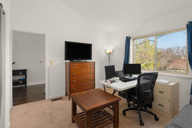 office space featuring baseboards, lofted ceiling, visible vents, and light colored carpet