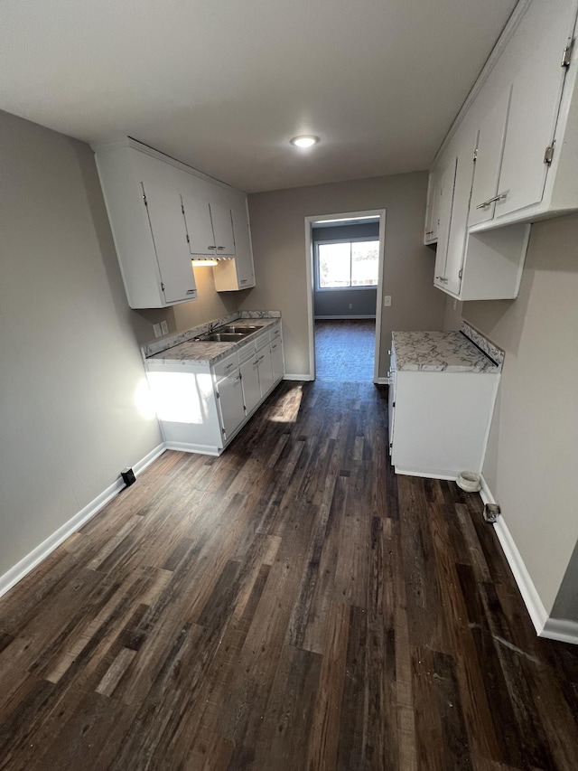 kitchen featuring a sink, white cabinetry, baseboards, light countertops, and dark wood finished floors