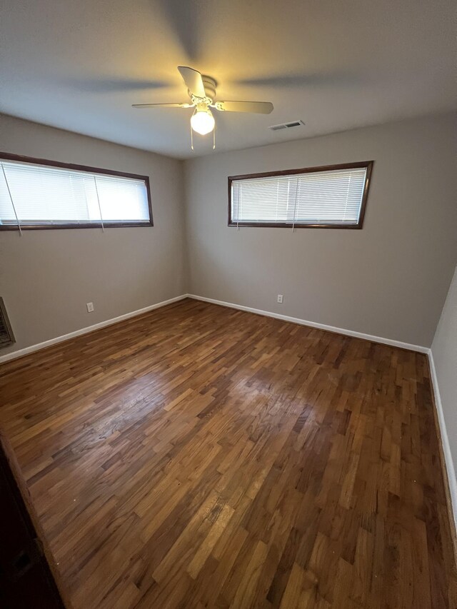 spare room featuring ceiling fan, dark wood-style flooring, visible vents, and baseboards