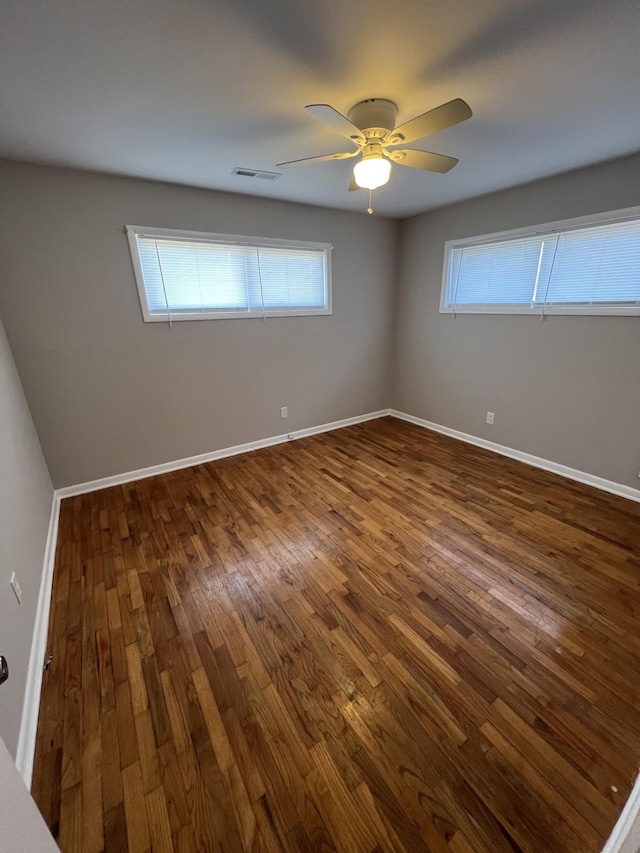 spare room featuring a ceiling fan, baseboards, visible vents, and dark wood-style flooring