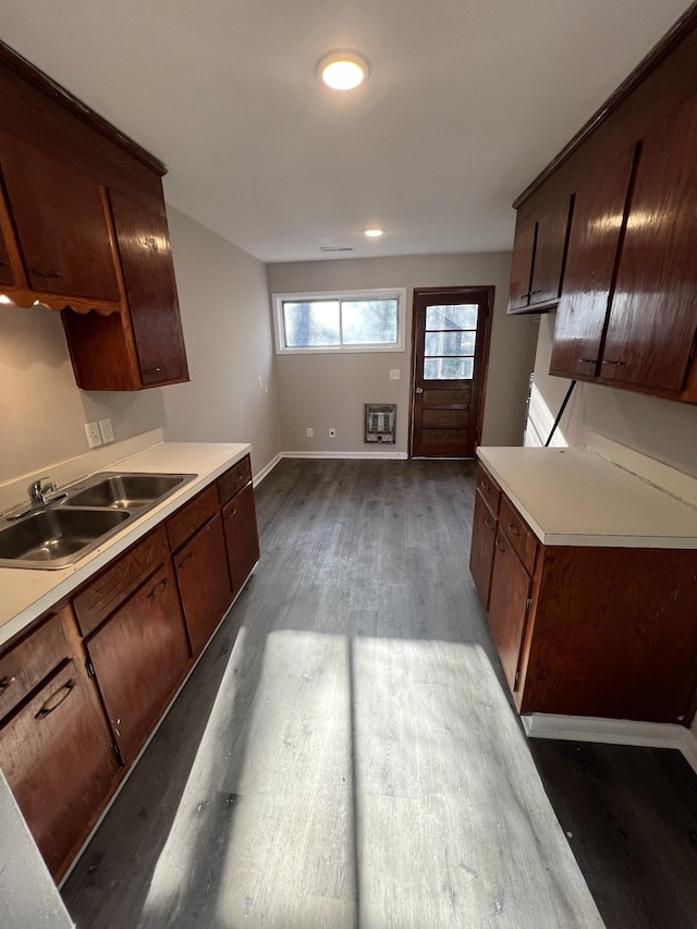 kitchen featuring dark wood-type flooring, a sink, baseboards, light countertops, and dark brown cabinets