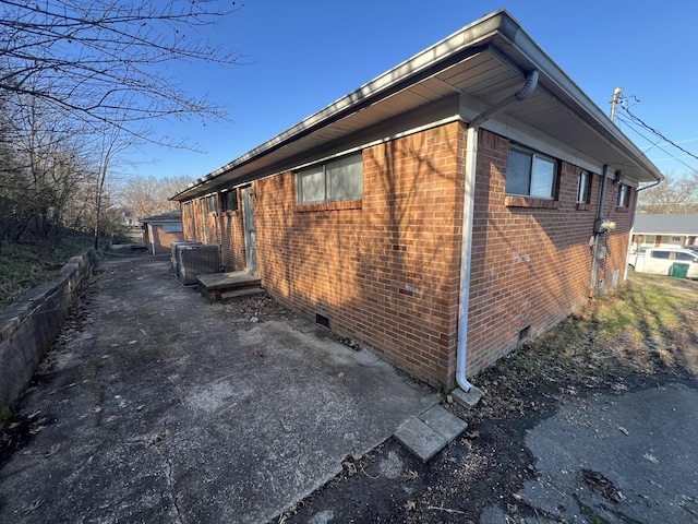 view of side of home featuring crawl space, central AC unit, and brick siding