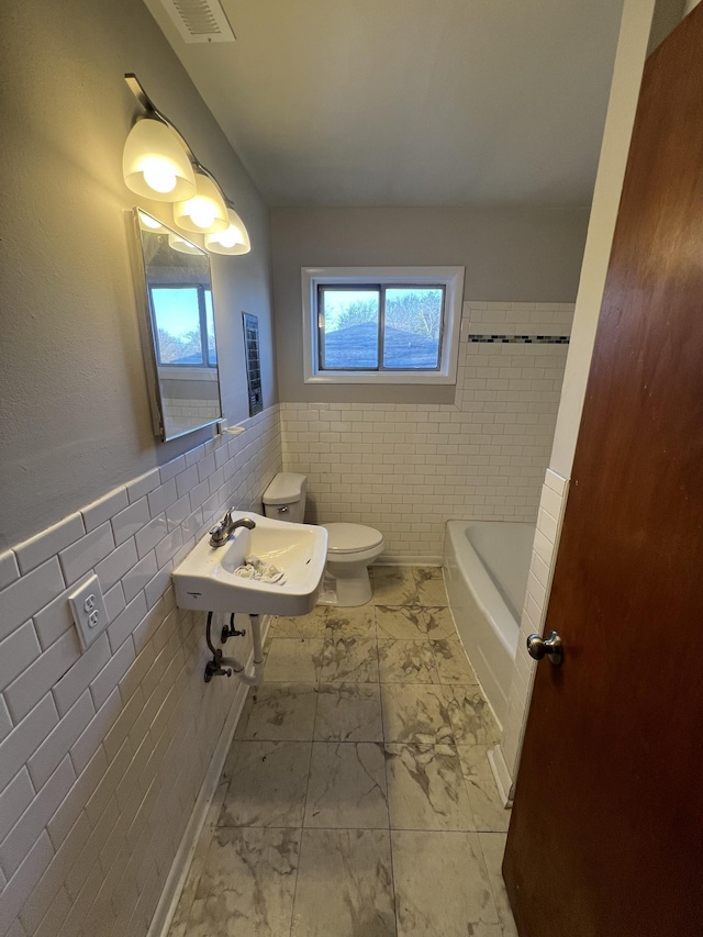 full bath with marble finish floor, tile walls, visible vents, a bathing tub, and a sink