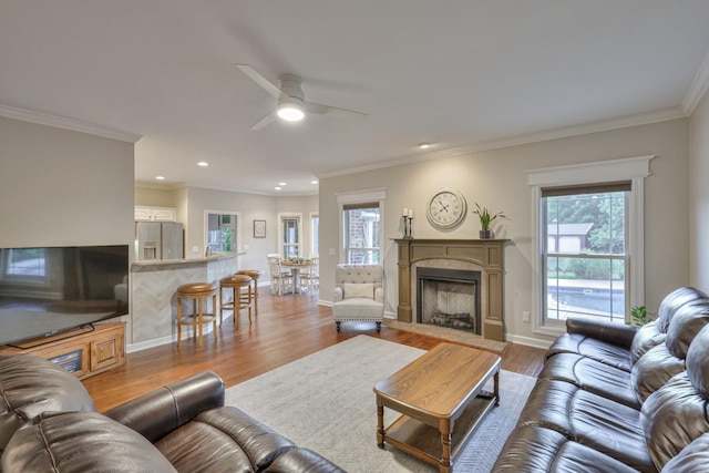 living room featuring baseboards, a fireplace with flush hearth, light wood-style flooring, and crown molding