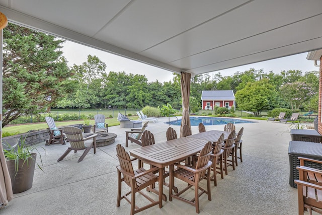 view of patio with a fire pit, an outbuilding, fence, and an outdoor pool