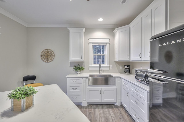 kitchen with light countertops, a sink, freestanding refrigerator, and white cabinets