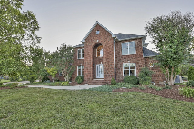 view of front of house featuring a front lawn, roof with shingles, and brick siding