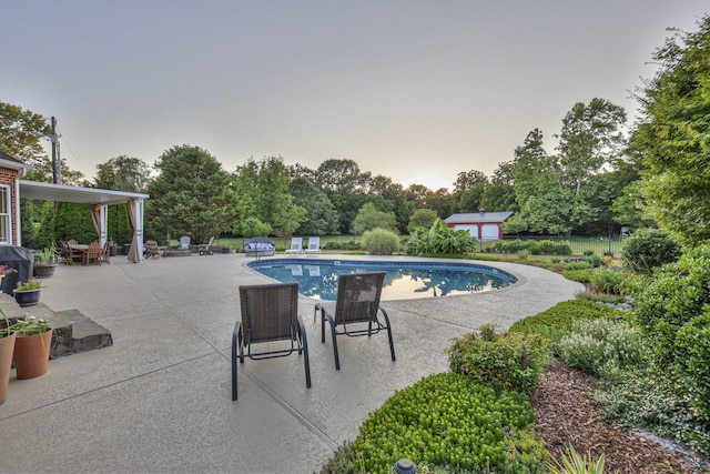 pool at dusk featuring a patio, fence, and an outdoor pool