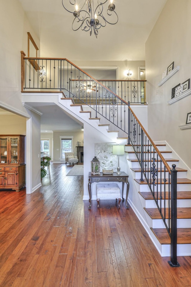 stairs with a chandelier, a high ceiling, wood finished floors, and baseboards