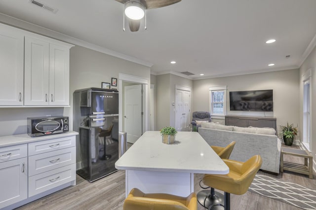 kitchen featuring a center island, a breakfast bar area, visible vents, freestanding refrigerator, and white cabinets