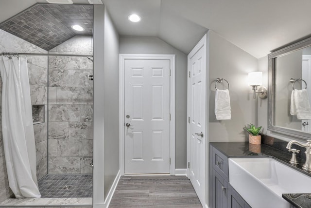 full bathroom featuring wood finished floors, vanity, baseboards, vaulted ceiling, and a shower stall